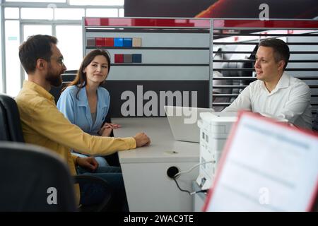 Spouses talking with manager in office area of car dealership Stock Photo