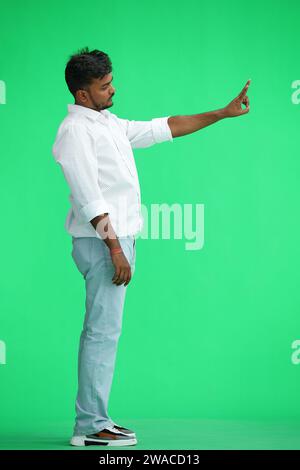 A man in a white shirt, on a green background, in full height, shows a victory sign, profile Stock Photo