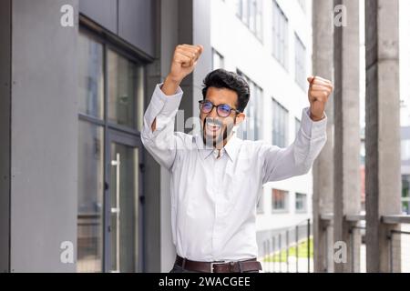 A joyful businessman dances from the outside of the office building, a satisfied man celebrates the victory of Triumph. Stock Photo