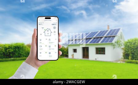 Hand holding smartphone with smart home app, monitoring solar panel energy, temperature, and home consumption, advancing the concept of efficient gree Stock Photo