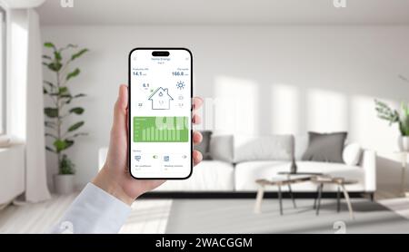 Hand holds phone displaying solar energy app in a cozy living room, effortlessly manage and monitor green power for sustainable living Stock Photo