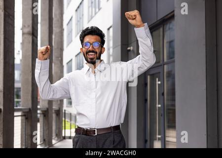 A joyful businessman dances from the outside of the office building, a satisfied man celebrates the victory of Triumph. Stock Photo