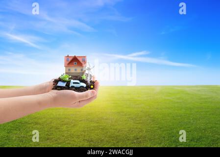 Hands cradle a sustainable home with solar panels, electric car, and wind generator, pioneering green living with eco-friendly homes and electric vehi Stock Photo