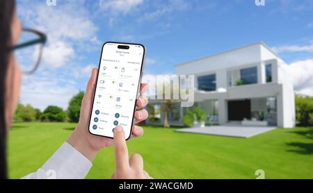 Woman controls temperature and home devices with a smart home app. Modern, eco-friendly house wih green yard in background Stock Photo