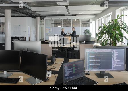 Two business people working together in IT office. In foreground are monitors with program code on them. Stock Photo