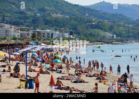 Summer day on a crowded beach in Cefalu with crystal blue water and green hills in the background. Stock Photo