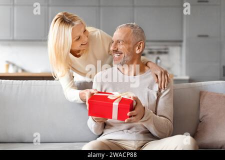Loving mature woman giving present her surprised husband Stock Photo