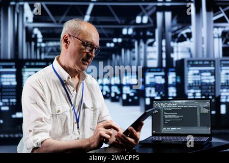 Senior engineer coding in high tech data center using javascript language. Expert updating software on server rigs on laptop terminal, ensuring optimal performance and security Stock Photo
