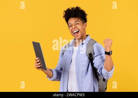 Exuberant black male student with tablet celebrating on yellow Stock Photo