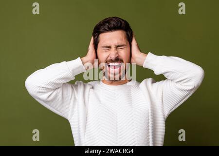 Photo of crazy mad furious man wear white trendy sweater cover ears loud sound scream isolated on khaki color background Stock Photo