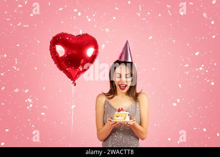 Delighted woman in a sequin dress with a party hat looking at a birthday cake Stock Photo