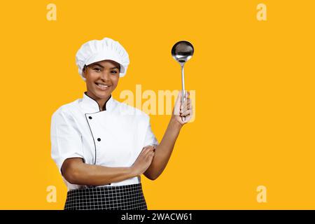 Beautiful young black female chef holding a ladle and smiling at camera Stock Photo