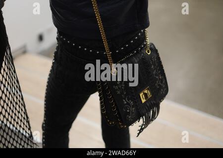 Woman in black silver stud jeans, studded belt and hand tooled black leather handbag with fringe, loop, stencilling with gold chain shoulder strap Stock Photo