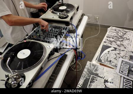 DJ working the decks, spinning vinyl at M2 art Gallery for a Graphic Art and Zines (on table) opening night event and party Stock Photo