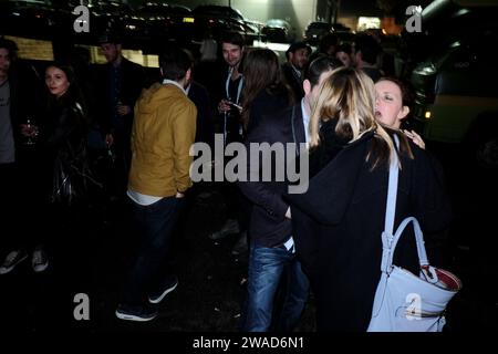 Groups of people standing in a dark poorly lit side street drinking outside a warehouse party in a gentrified inner city industrial area in  Sydney Stock Photo