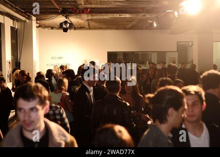 People attending a Richard Kern art opening in Sydney, looking across a large warehouse art space with exposed rafters, spotlights, conversations Stock Photo