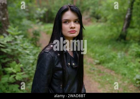 Portrait of thoughtful woman in leather jacket while standing in forest Stock Photo