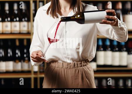 Female sommelier pouring red wine into long-stemmed wineglass, close up indoor portrait. Stock Photo