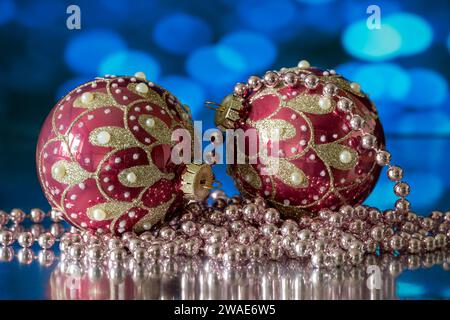 A pair of red and gold Christmas Tree baubles, photographed with a white beaded necklace, against a blue background Stock Photo