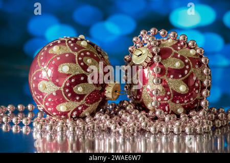 A pair of red and gold Christmas Tree baubles, photographed with a white beaded necklace, against a blue background Stock Photo