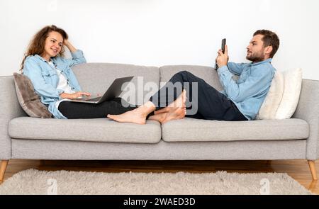Woman and man relax on sofa and using their digital portable information devices. Stock Photo