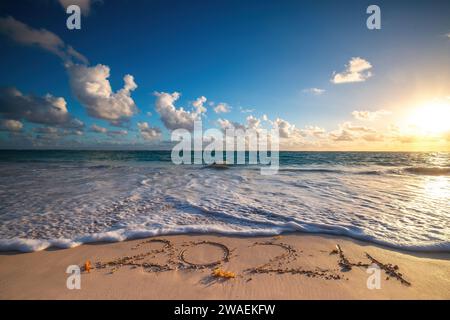 Island beach sea sunrise and text happy new year 2024 on the sand Stock Photo