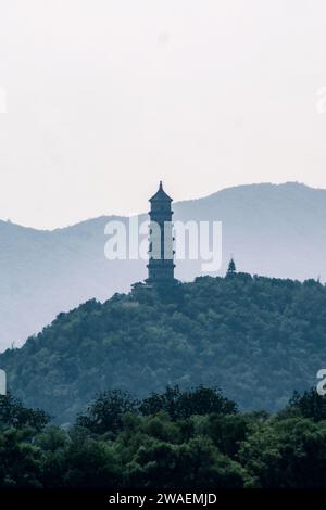 A majestic ivory-hued tower stands atop a rolling green hill dotted with lush trees. Stock Photo