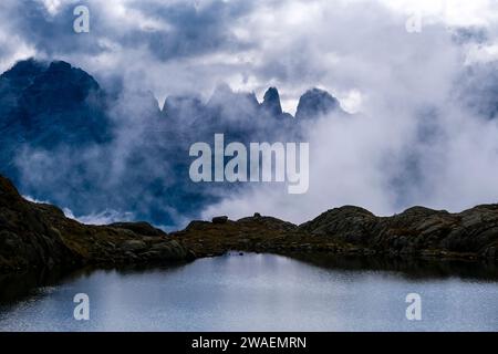 The main range of Brenta Dolomites, partly covered in clouds, seen from the lake Lago Nero. Stock Photo