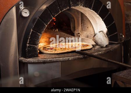 Perfectly Cooked Pizza Emerging from a Modern Wood-Fired Oven Stock Photo