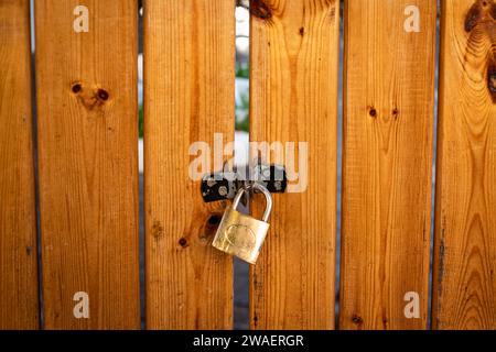 Wooden gate of the home garden. The gate is closed with a padlock. Metal padlock securing a wooden gate. Locker on wooden door. Nobody, street photo Stock Photo
