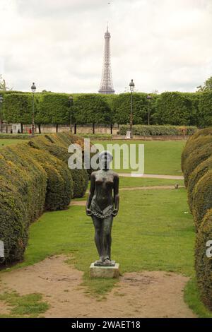 A majestic bronze statue stands tall in front of a pair of lush green hedges, with the iconic Eiffel Tower in the background Stock Photo