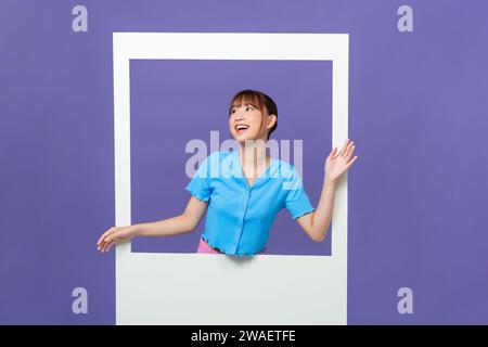 Photo of shiny funny young lady smiling looking through white window isolated on purple background Stock Photo