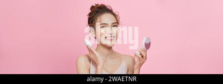 Young attractive lady applying cushion on her face with powder puff on pink background Stock Photo