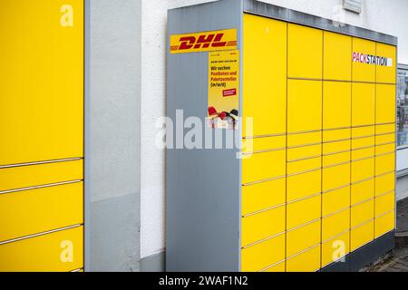 Innovative Paketlogistik - Nutzung der DHL Packstation 04.01.2024, Bad Camberg: Symbolfoto, Illustrationsbild, Symbolbild, Illustrationsfoto Das Bild zeigt eine Frau im Anschnitt, die mit ihrem Smartphone über den Touchscreen einer DHL Paketstation interagiert, um ein Paket einzureichen. Sie ist konzentriert auf die digitale Schnittstelle fokussiert, während ihre Hand das Mobiltelefon hält und die entsprechenden Eingaben auf dem Bildschirm der Paketstation tätigt um das Paket einzulegen. Die Packstation, ein Paketautomatensystem von DHL, bietet seit 2001 in über 12.500 Standorten deutschlandwe Stock Photo