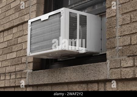 exterior view of air conditioning window unit extruding from the window sill of a brown brick building Stock Photo