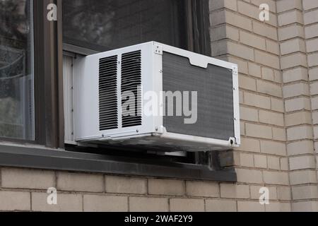 exterior view of air conditioning window unit extruding from the window sill of a beige brick building Stock Photo