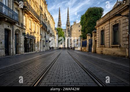 Street in the centre of Bordeaux with the tramway tracks, historic houses and St. Andrew's Cathedral at the end at sunset. Stock Photo