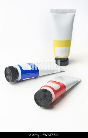 scattered artist's paint tubes with black cap isolated on white background, art supplies of primary colors blue, yellow and red, mock-up template Stock Photo