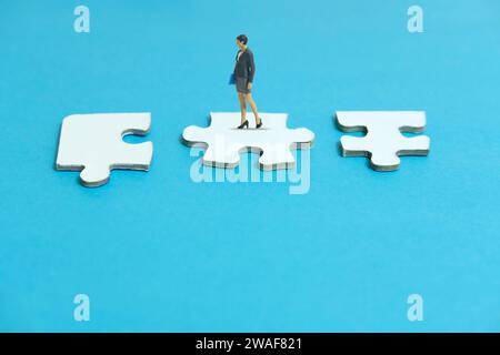 Miniature people toy figure photography. A businesswoman standing above three piece puzzle jigsaw. Isolated on blue background. Image photo Stock Photo