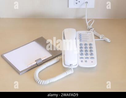 Telephone with note paper and pencil near bed is served for guests in hotel room. Stock Photo