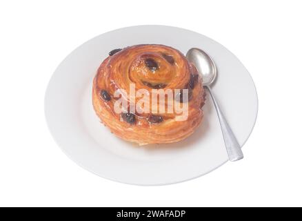 Spiral danish pastry or sweet bun with raisin on top on white plate with small teaspoon served for breakfast is isolated on white background. Stock Photo