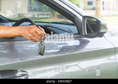 Seller is handing over a key remote control to buyer from inside the car at showroom on delivery day after driving demonstration or test. Stock Photo