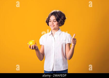 Girl holds an oranges in hand and shows thumbs up gesture. Healthy food, vitamins and children nutrition concept Stock Photo