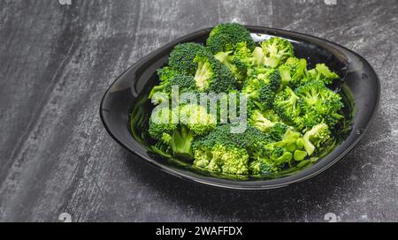 Fresh green broccoli florets in black bowl isolated on gray background, side view Stock Photo