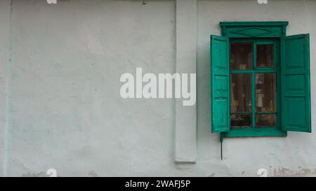 window with green wooden shutters on the plastered facade of an old house on the right side of the wall, an empty space on a light surface on the left Stock Photo