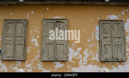 three windows closed with old shabby shutters on a shabby wall of an ancient house as a vintage texture background in brown tones Stock Photo
