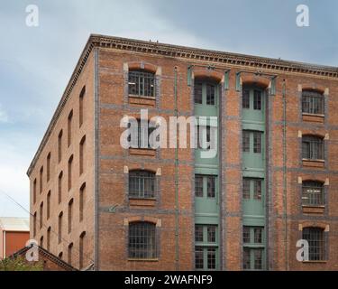 Exterior of an old red brick multi level warehouse, featuring metal loading doors. Stock Photo