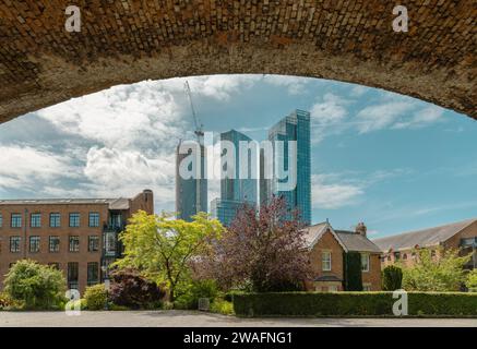 Framed by a railway bridge, the contemporary architecture of Manchester skyscrapers is seen rising up above more traditional housing. Stock Photo