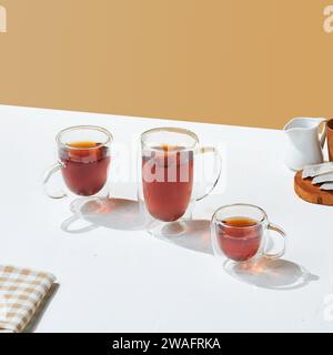 a variety size of transparent double wall glass with tea inside it, on a white and beige colored background. Stock Photo
