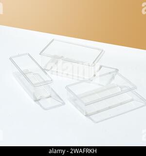 A plain transparent plastic food container, on a white and beige colored background. Stock Photo